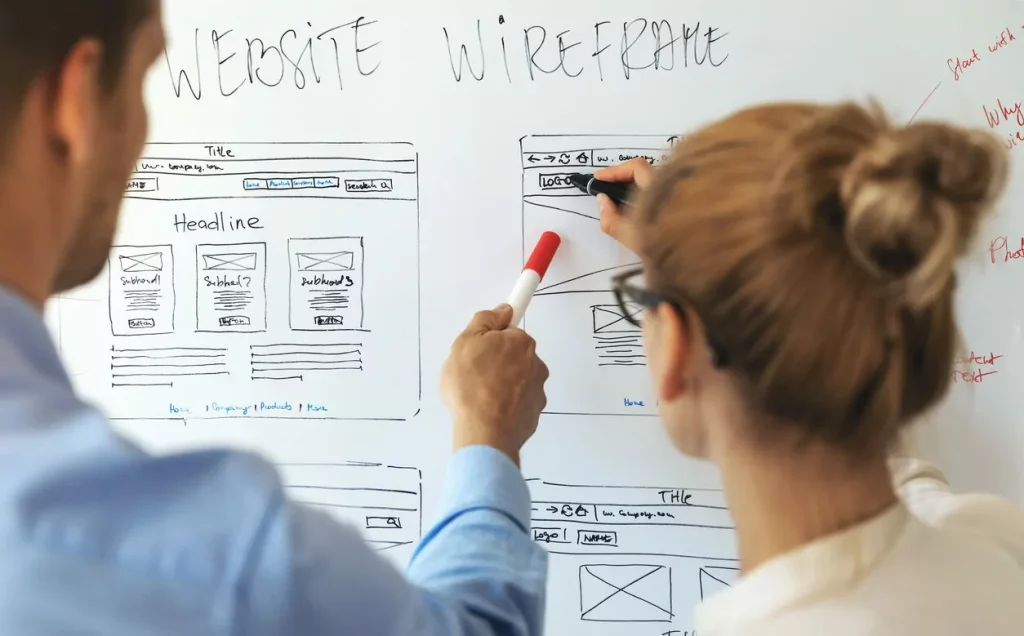 Two designers sketching a website wireframe on a whiteboard during UX design
