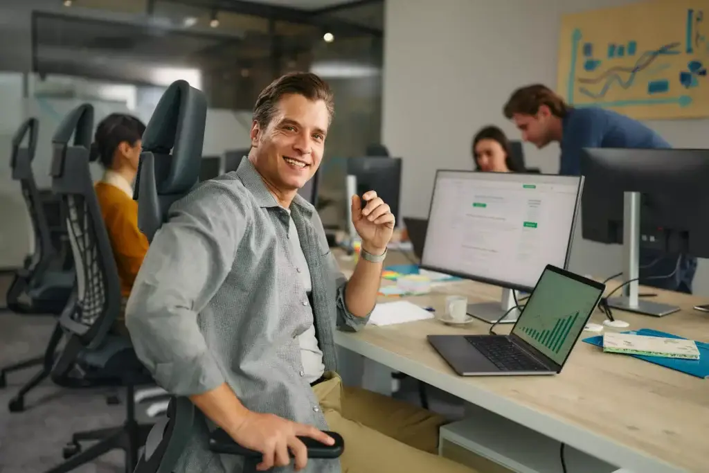 Smiling man at an office desk with colleagues at computers, illustrating site optimization with analytics